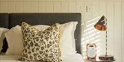 A bed with a grey headboard, floral pillows and a small side table to the right that has a radio and a lamp ontop.