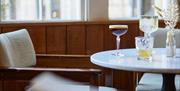 A table with cocktails and a small vase. There is a beige coloured chair tucked under the table