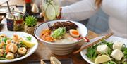 Various japanese dishes on a table: including a ramen bowl with an egg and meat, a prawn dish, and a salad.