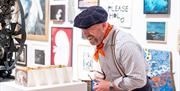 A man in a striped shirt, neckerchief and beret looking at a concertina card display in a modern art gallery