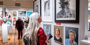 A lady with long silver hair looking at varied portraits in a modern art gallery