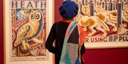 A lady wearing a colourful scarf and blue beret looking at prints of an owl and wolves.