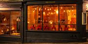 The exterior of The Village cafe and bar. Six red bar stools are visible in a row against the window.