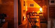 Multiple tables, chairs and a wall-length cushioned bench in a warmly-lit dining area