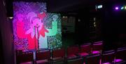 An empty dark stage with two rows of chairs and a jester cartoon backdrop.