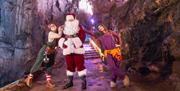 A person dressed as Father Christmas, flanked by two performers from the Wookey Hole Circus, in a cave.