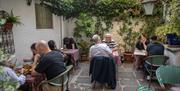 Al fresco dining at Yak Yeti Yak, featuring customers sat around brightly coloured tables and chairs. The far wall of the garden is lined with tall po