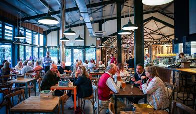 Indoor farm shop cafe with dark ceiling beams, hanging lights and wooden table and chairs