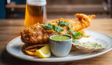 A plate of fish, chips and sauces with a pint of beer in the background at The Scallop Shell in Bath