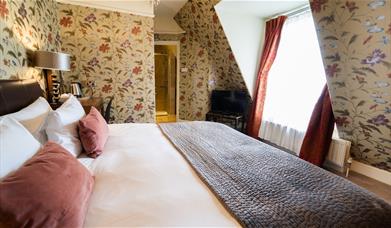 A hotel room with double bed, TV and floral wallpaper