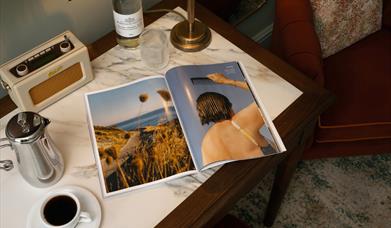 An image of a table with a magazine, radio, coffe mug and jug.
